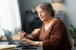 Ältere Frau, die Laptop verwendet, der am Schreibtisch im Wohnzimmer sitzt