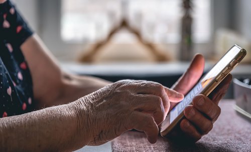 Hände einer älteren Frau, die ein Mobiltelefon hält